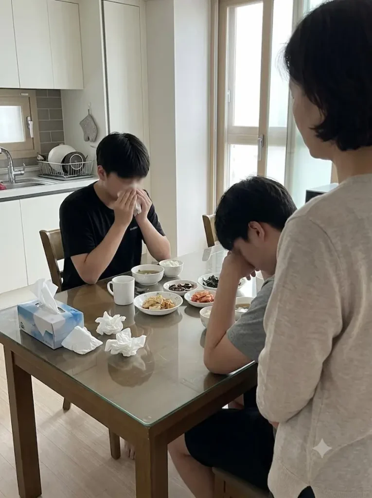 아침 식탁에서 코막힘으로 인해 휴지로 코를 훌쩍이며 힘들어하는 아들과 이를 걱정스레 바라보는 부모의 일상 사진
