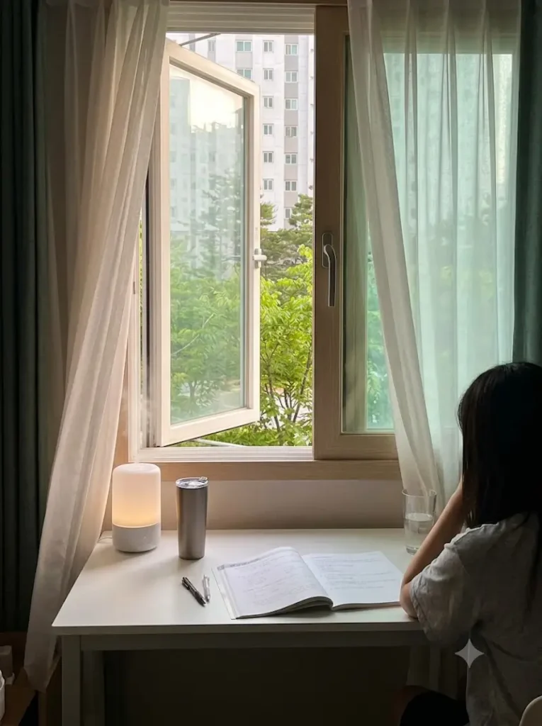 공부방 창문이 활짝 열려 쾌적하게 환기가 되고 있는 창가 책상과 텀블러, 그리고 잠시 휴식을 취하고 있는 수험생의 뒷모습